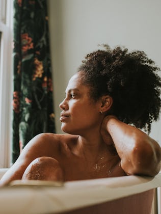A beautiful woman bathes in a roll top bath. She seems distracted as she rests her head on her arm a...