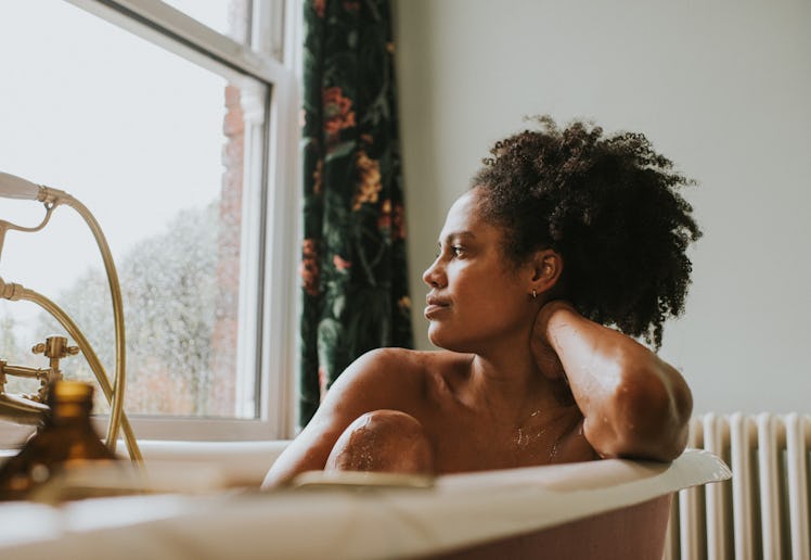 A beautiful woman bathes in a roll top bath. She seems distracted as she rests her head on her arm a...