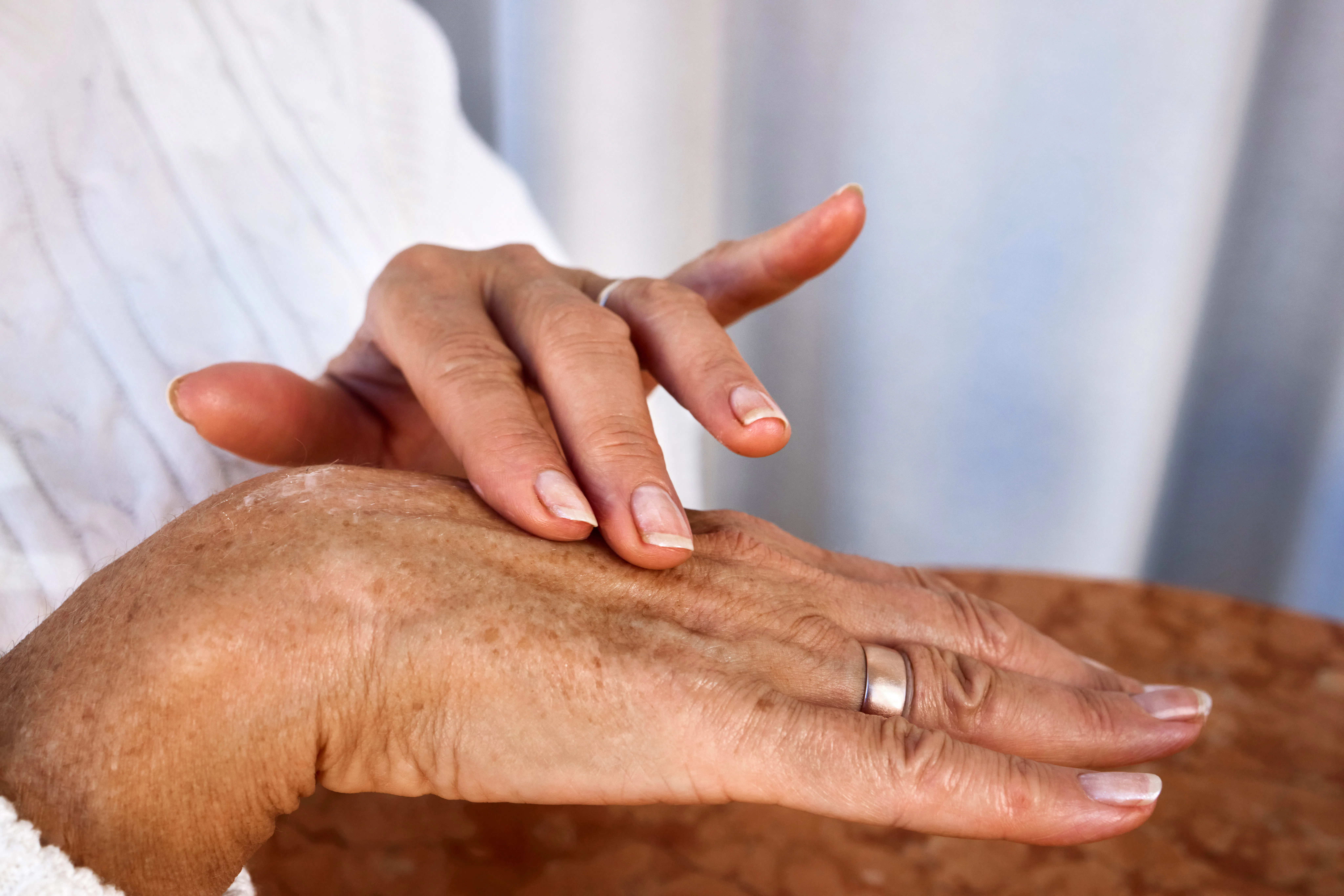 Elderly hands with age spots and wrinkles applying moisturizing cream, close-up of daily skincare ro...