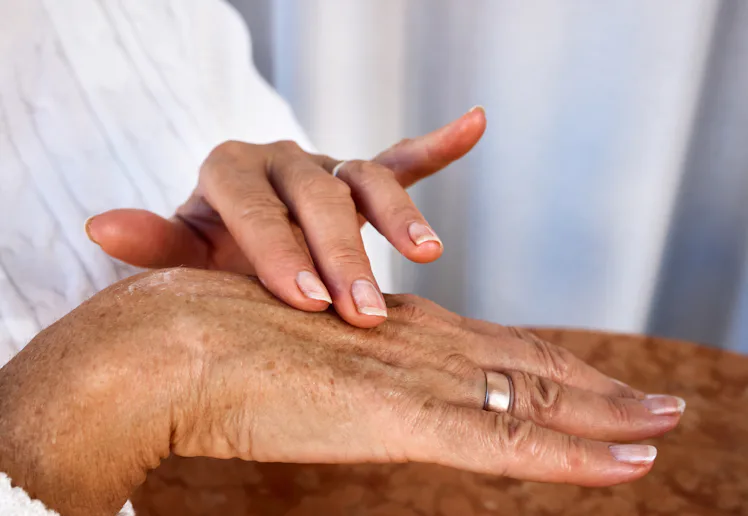 Elderly hands with age spots and wrinkles applying moisturizing cream, close-up of daily skincare ro...