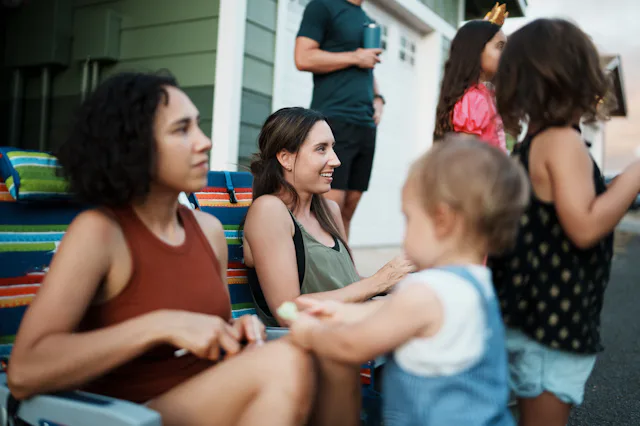 A pretty woman sits in a beach chair in front of her home and smiles while watching a Halloween para...
