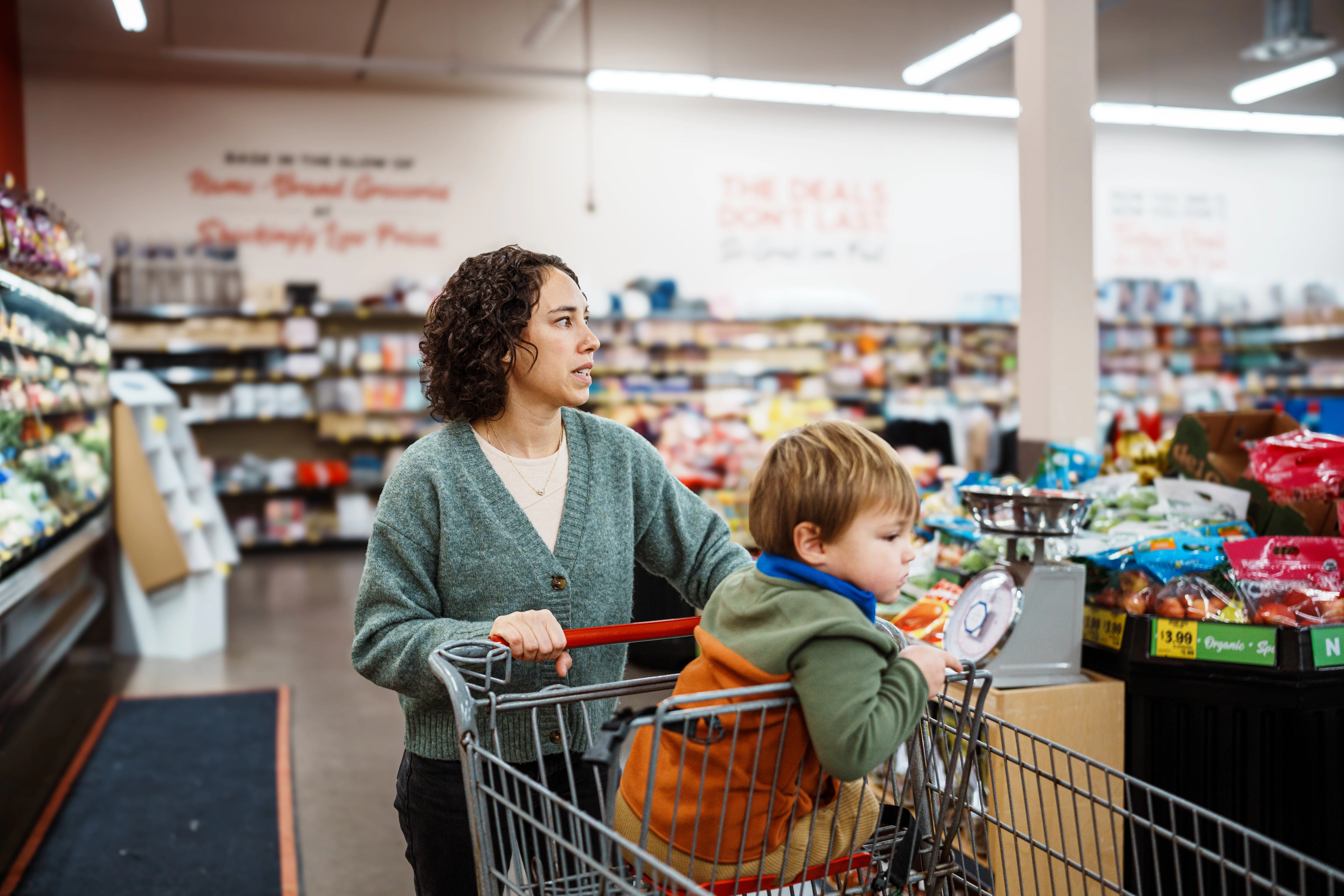 An Eurasian woman pushes her two year old son in a shopping cart through the produce section of a gr...