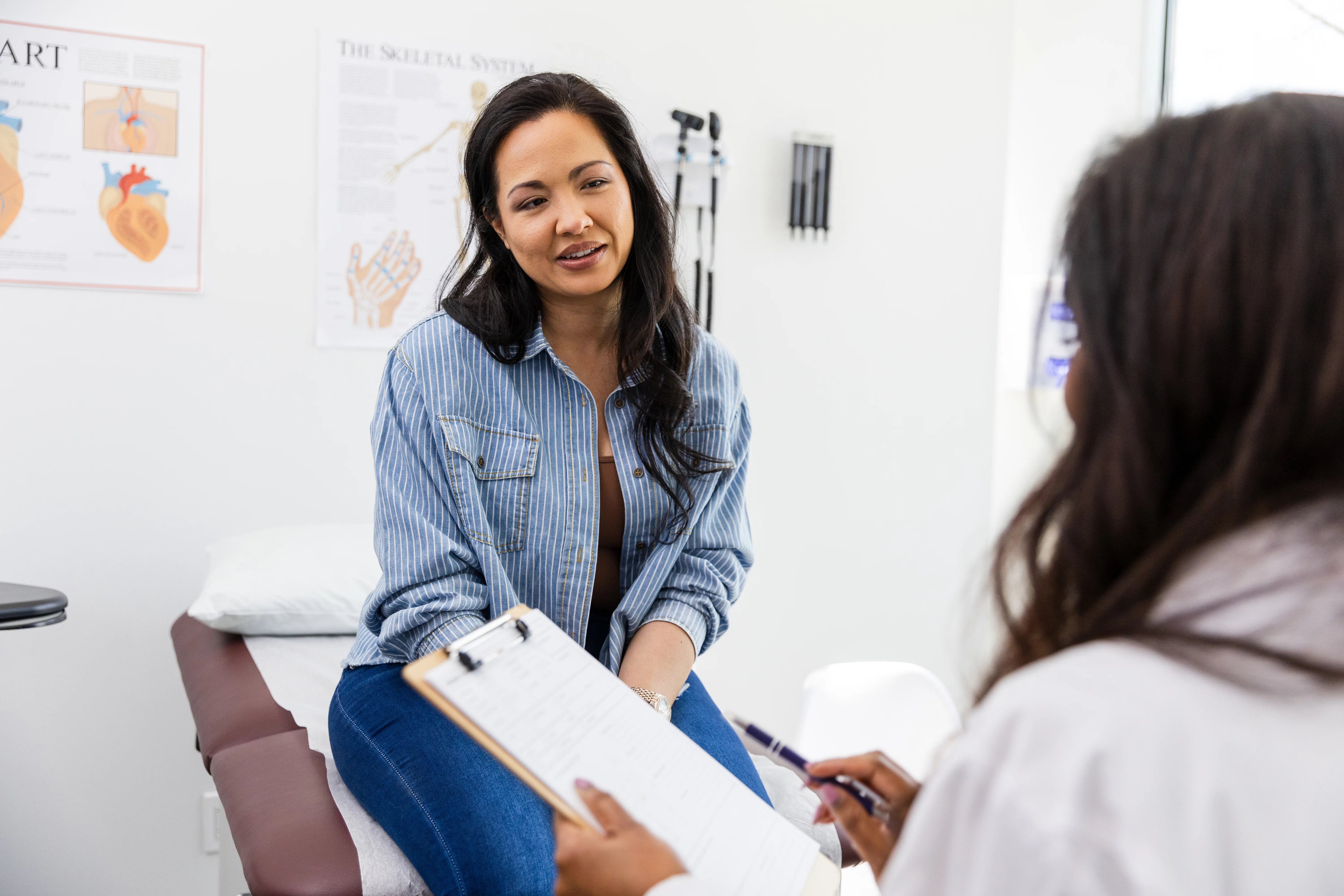 The unrecognizable female doctor reviews the patient's medical history while she sits on the examina...