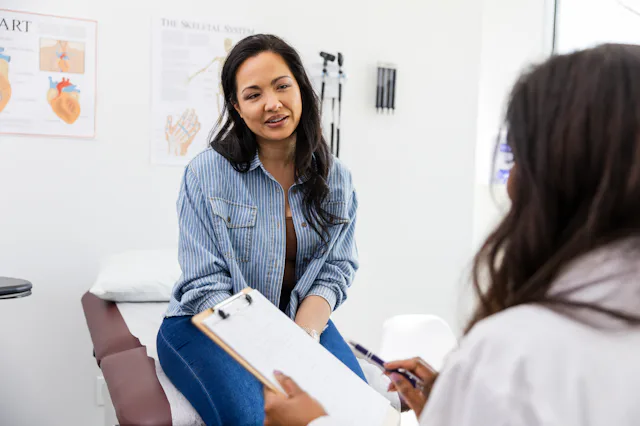 The unrecognizable female doctor reviews the patient's medical history while she sits on the examina...