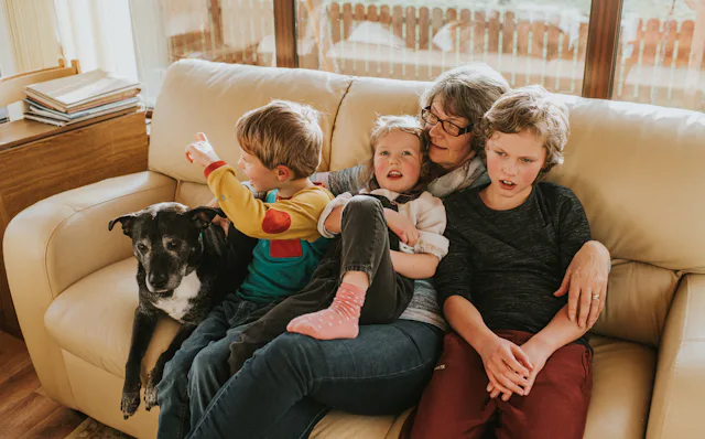 A grandmother is surrounded by her young grand children on a leather sofa. Her grand daughter sits o...