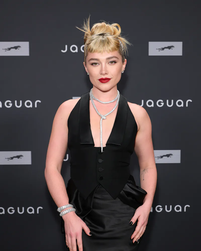 Florence Pugh at a Jaguar event with a top knot, red lip, and crystal nail art