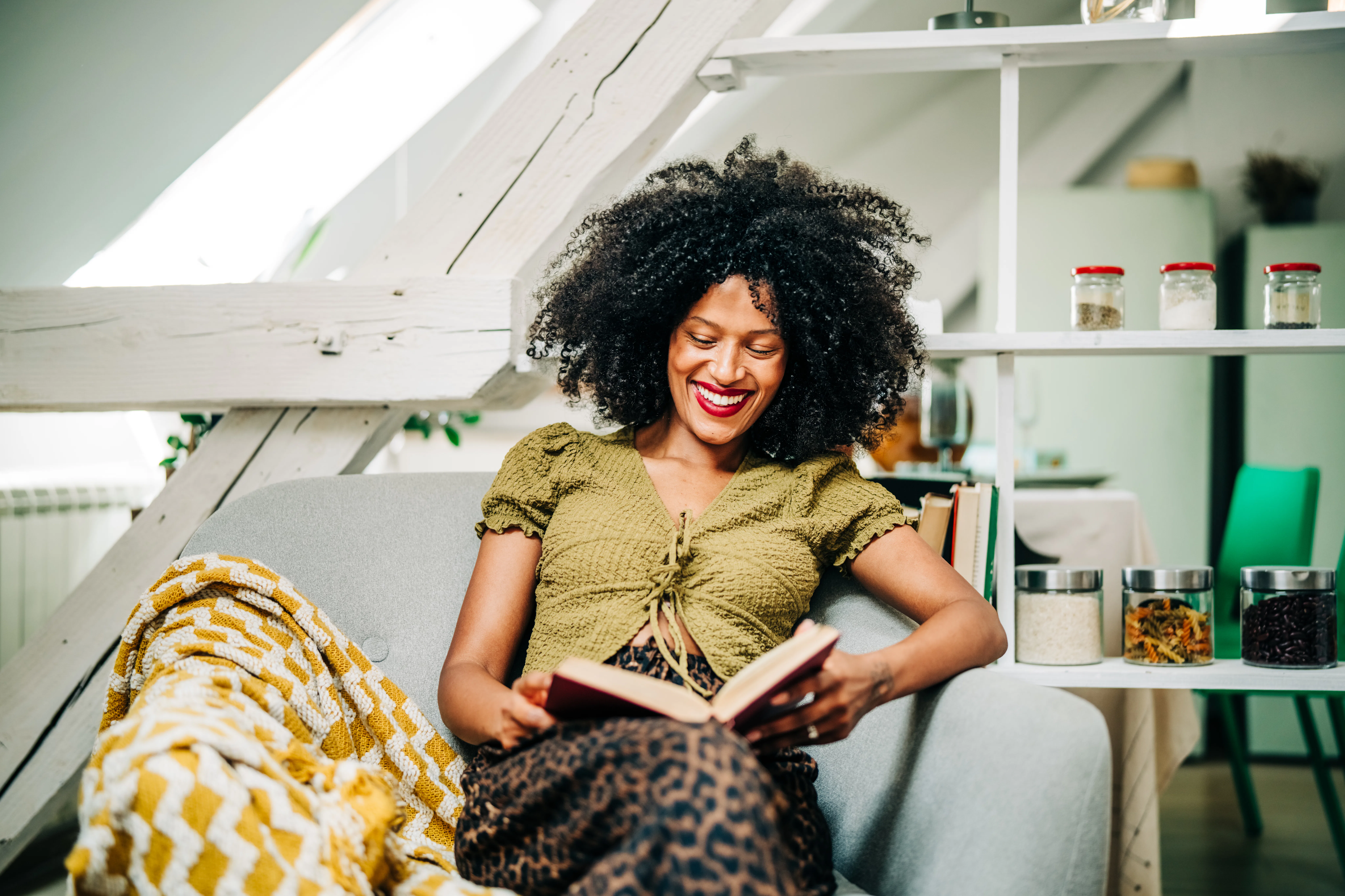 A young woman drinks tea while relaxing and reading a book in the living room.