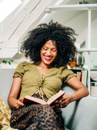A young woman drinks tea while relaxing and reading a book in the living room.