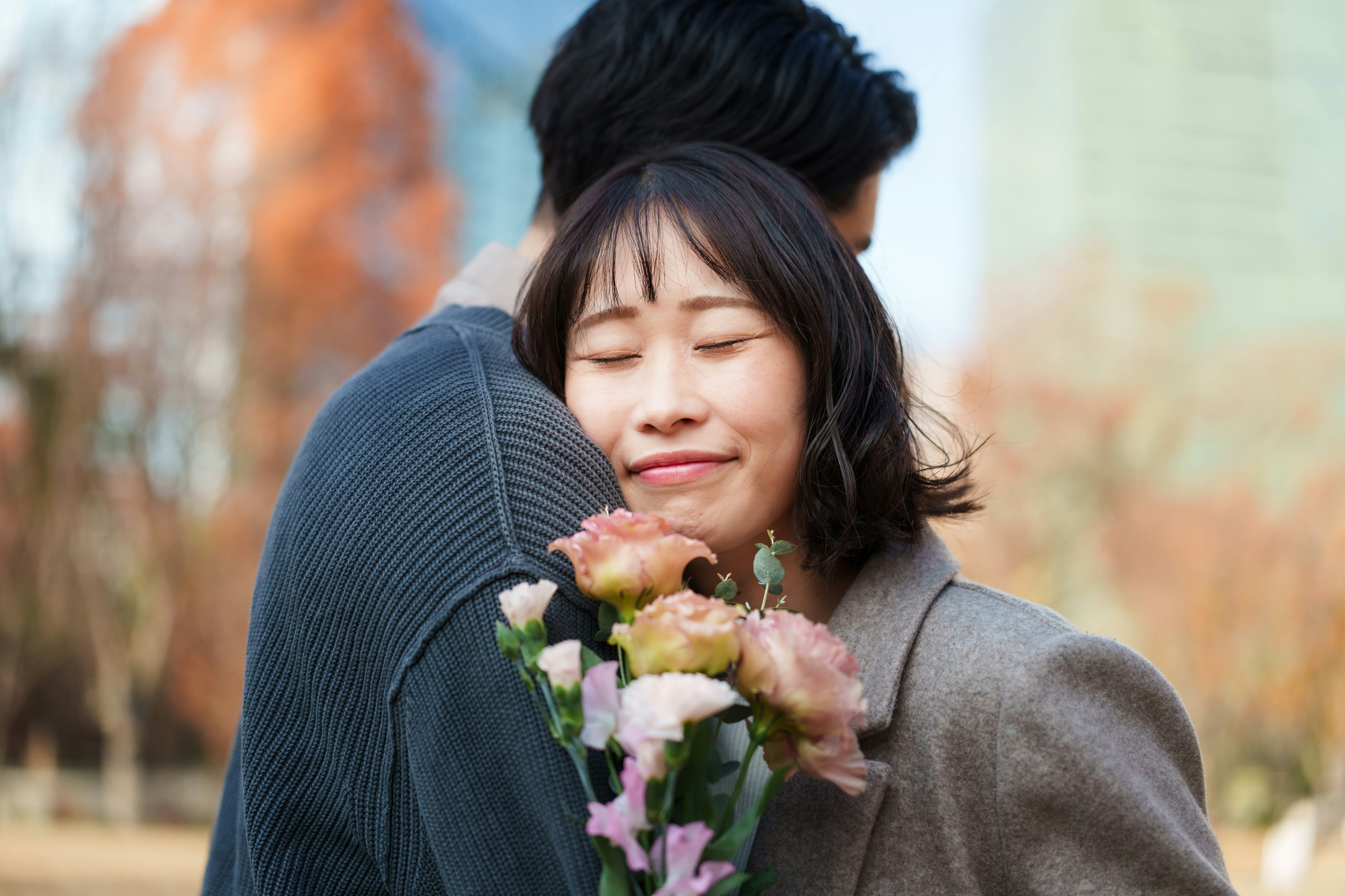 Young woman gently holds a bouquet of flowers while leaning into her partner, smiling with her eyes ...