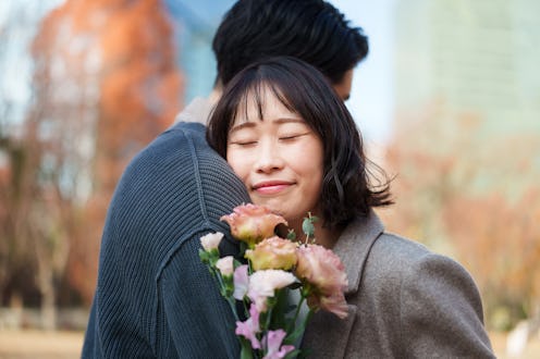 Young woman gently holds a bouquet of flowers while leaning into her partner, smiling with her eyes ...