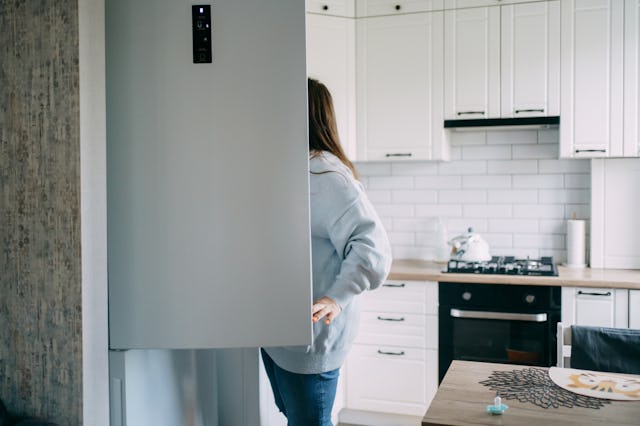 Young woman searching for food inside her refrigerator in a modern white kitchen