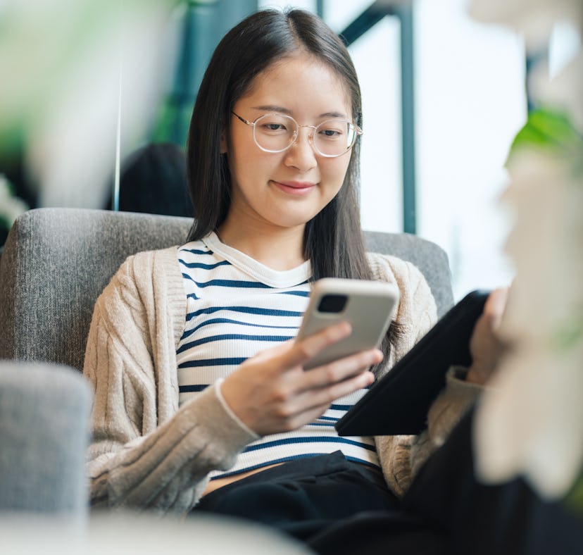 Closeup of a gen zwoman’s hand using a smartphone highlights the tactile connection between people a...