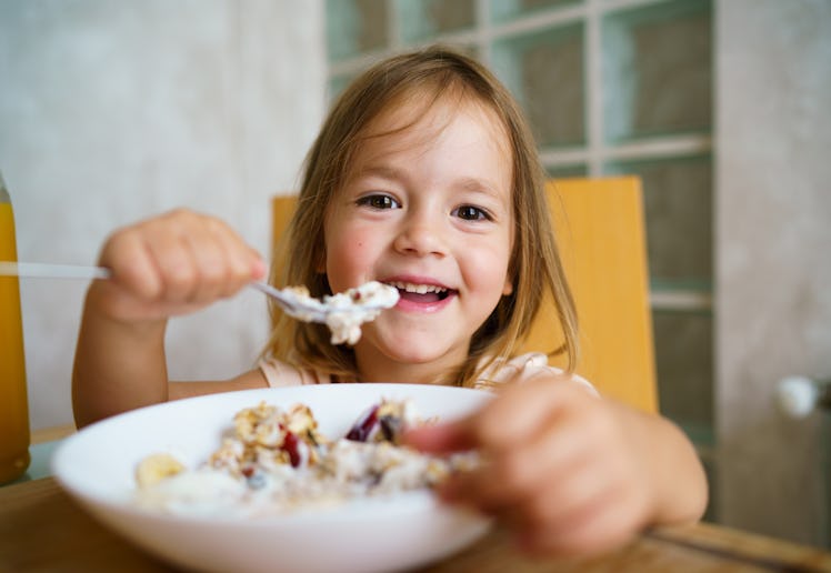 A little girl eats a bowl of oatmeal.