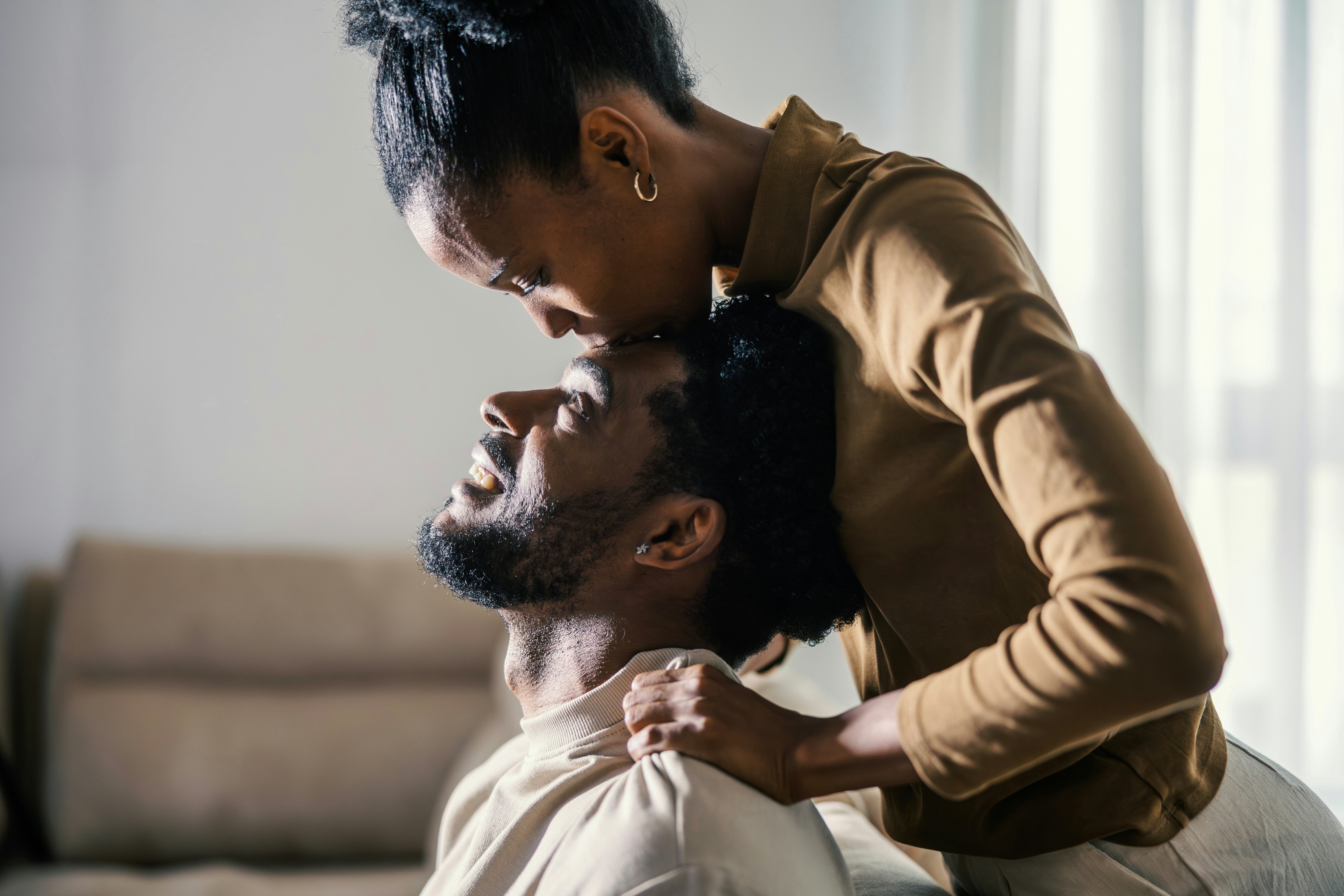 Woman showering her happy boyfriend with a tender forehead kiss, expressing love and intimacy in the...