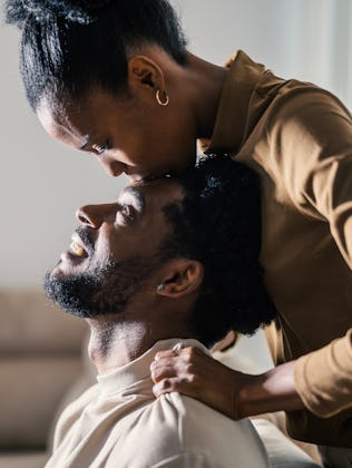 Woman showering her happy boyfriend with a tender forehead kiss, expressing love and intimacy in the...