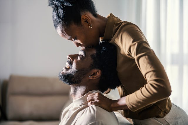 Woman showering her happy boyfriend with a tender forehead kiss, expressing love and intimacy in the...
