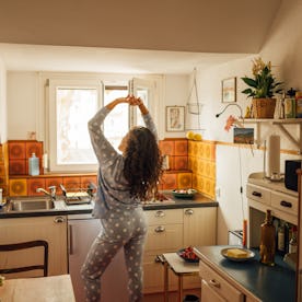 A woman in polka dot pajamas stretches by the kitchen window, enjoying a quiet morning. Warm light a...