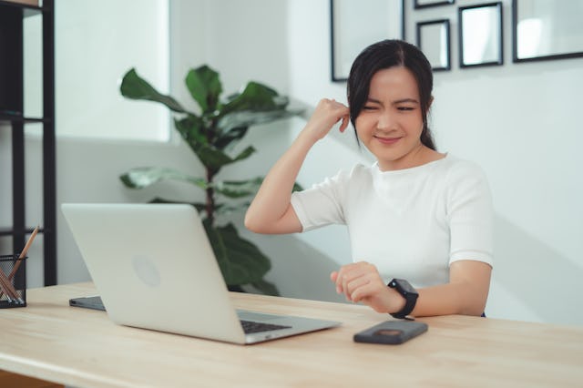 Asian woman itching from ear inflammation and putting a finger into her ear sitting at home office.