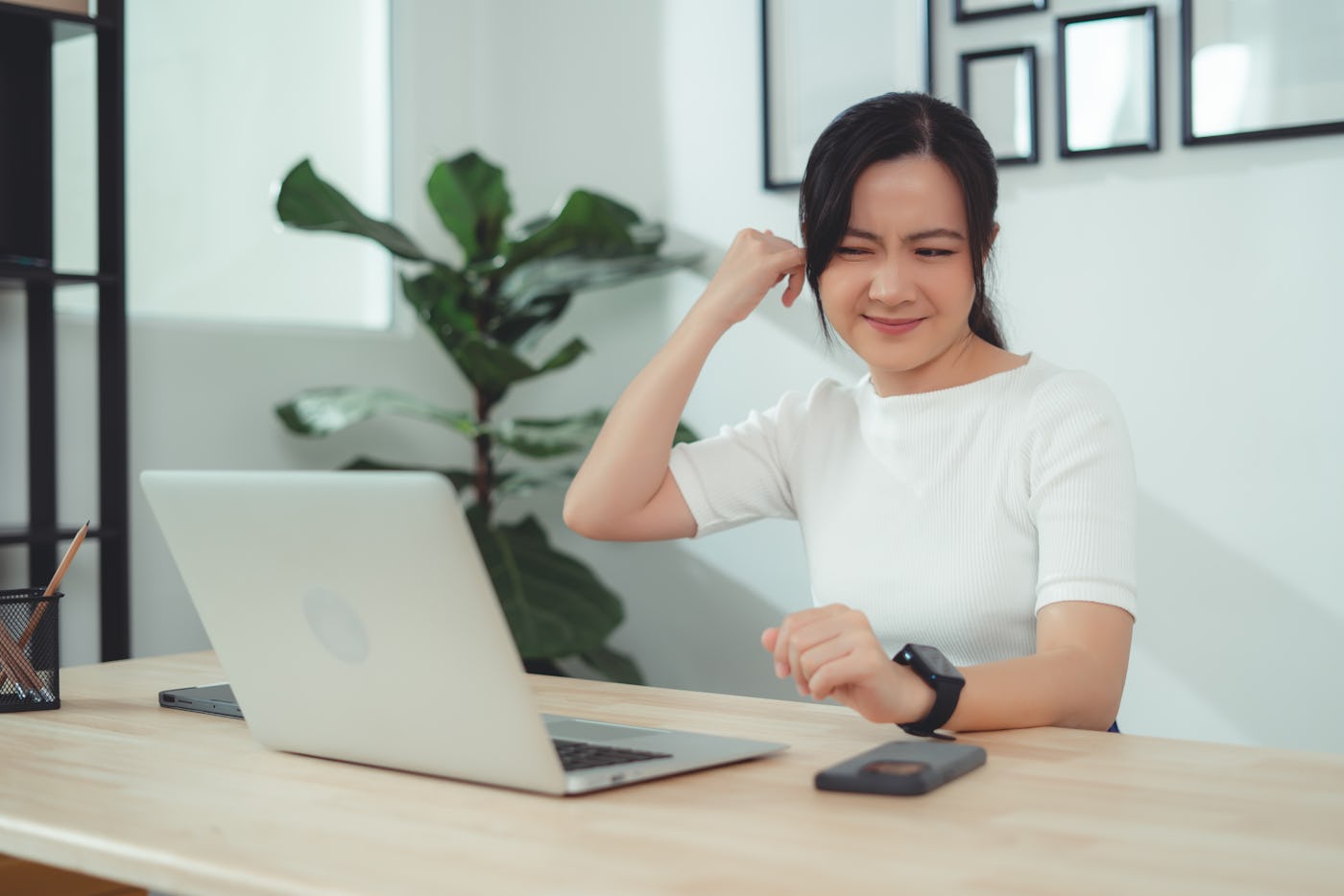 Asian woman itching from ear inflammation and putting a finger into her ear sitting at home office.