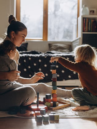 Young Mother playing with children while sitting on floor at home with wooden toys