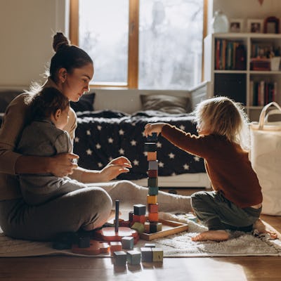 Young Mother playing with children while sitting on floor at home with wooden toys