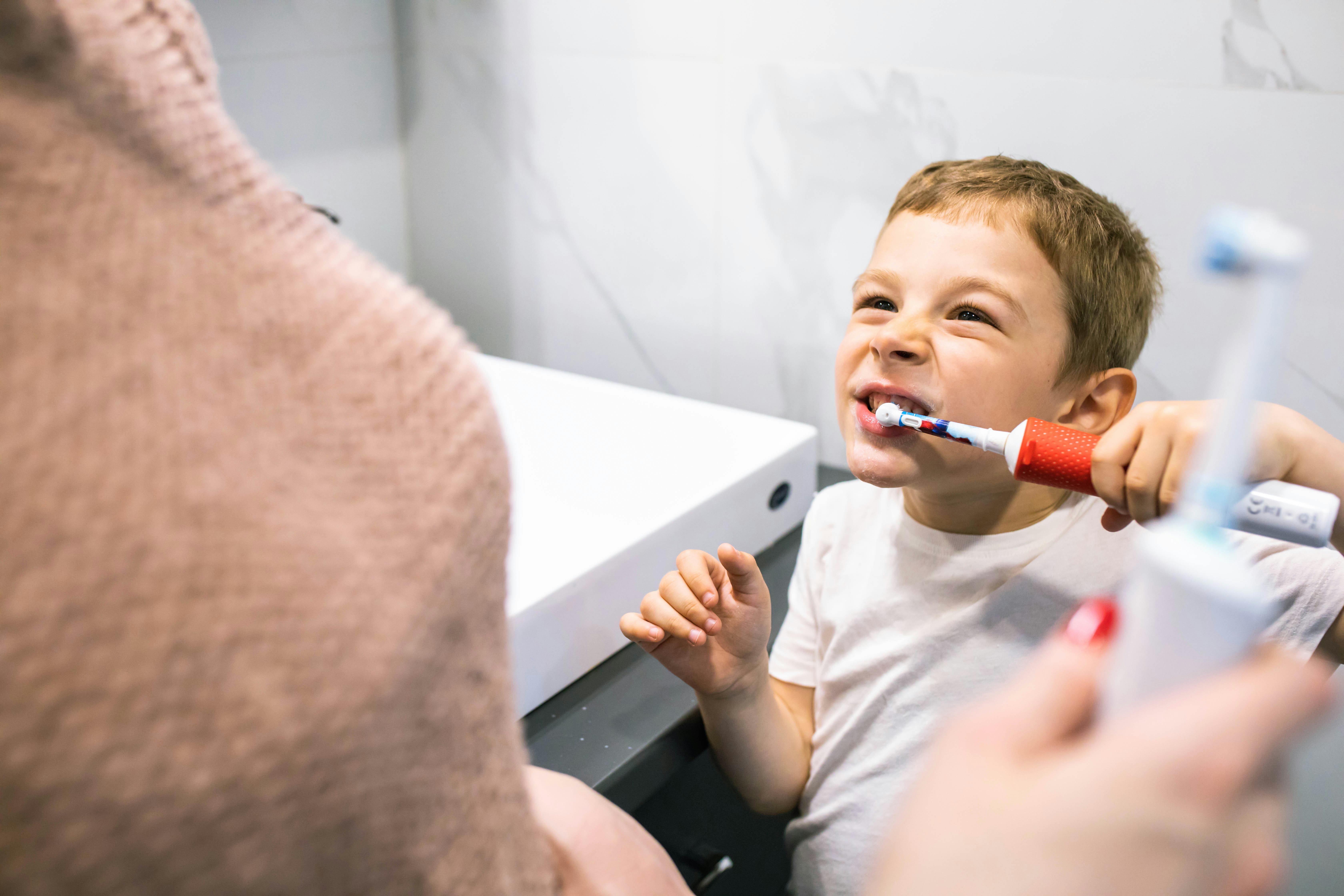 A cute boy and his mom are brushing their teeth with electric toothbrushes