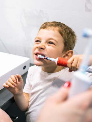 A cute boy and his mom are brushing their teeth with electric toothbrushes