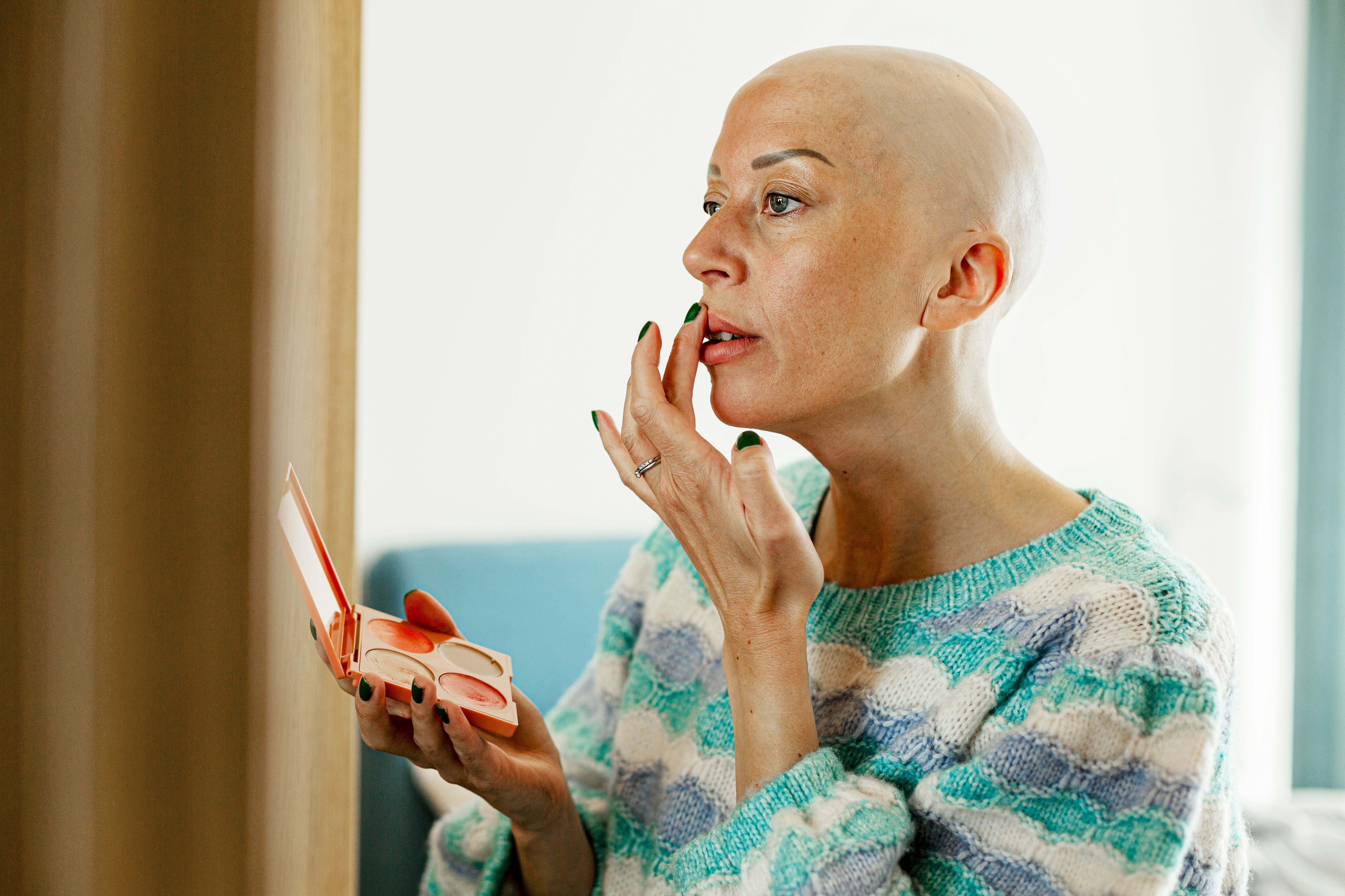 Bald mature woman applying lipstick at home