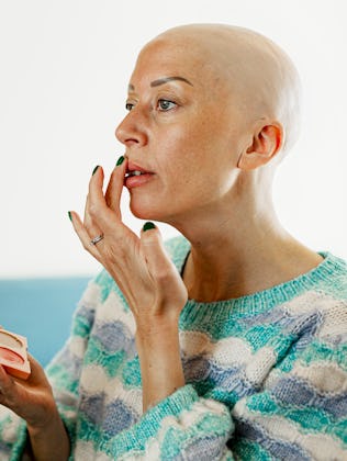 Bald mature woman applying lipstick at home