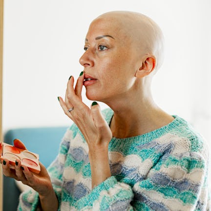 Bald mature woman applying lipstick at home