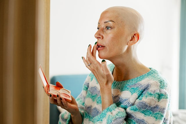 Bald mature woman applying lipstick at home
