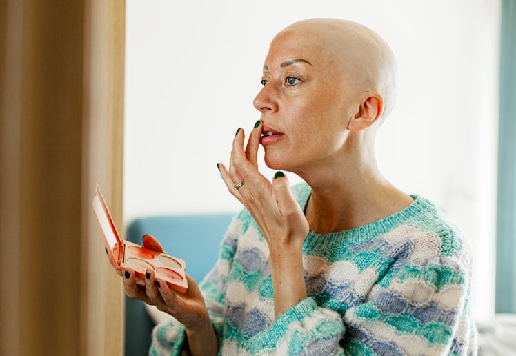 Bald mature woman applying lipstick at home