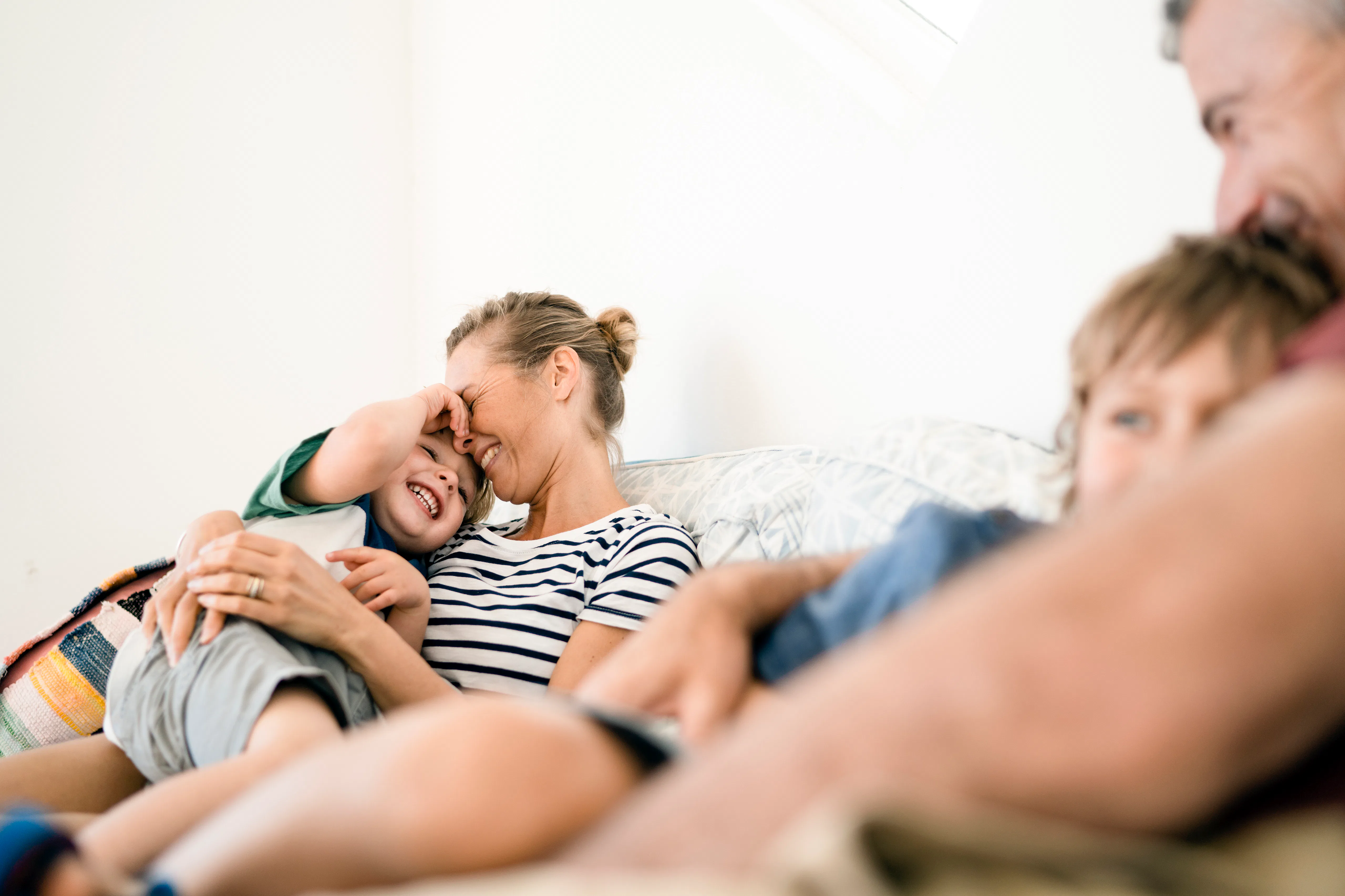 A photo of smiling family relaxing on sofa. Happy parents are embracing sons. They are wearing casua...