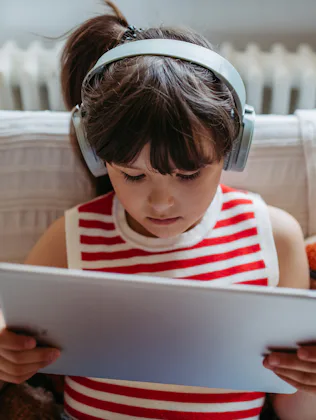 Portrait of a young girl watching a video on a tablet with wireless headphones on. Girl spending her...