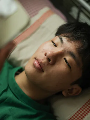 While in bed an Asian teenager with Type 1 Diabetes checks his mobile app monitor to determine his i...