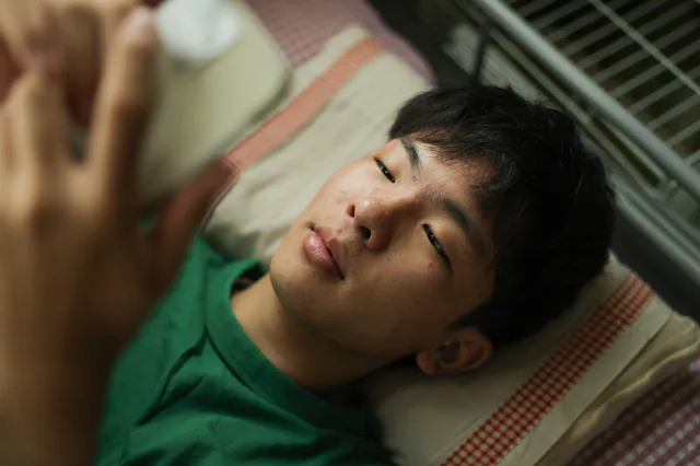 While in bed an Asian teenager with Type 1 Diabetes checks his mobile app monitor to determine his i...