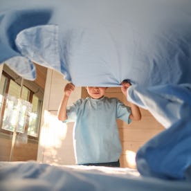 A boy in a blue T-shirt is making his bed.