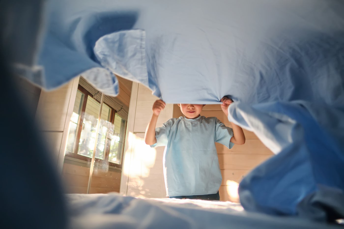 A boy in a blue T-shirt is making his bed.