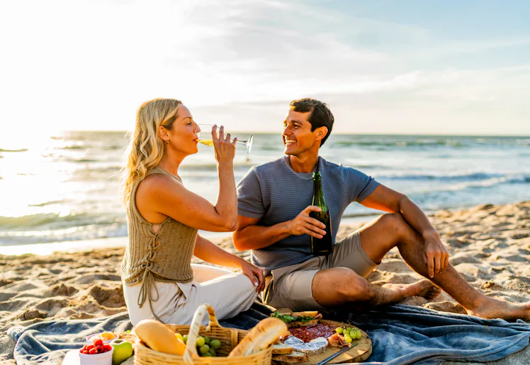 Couple talking and drinking wine during picnic on the beach