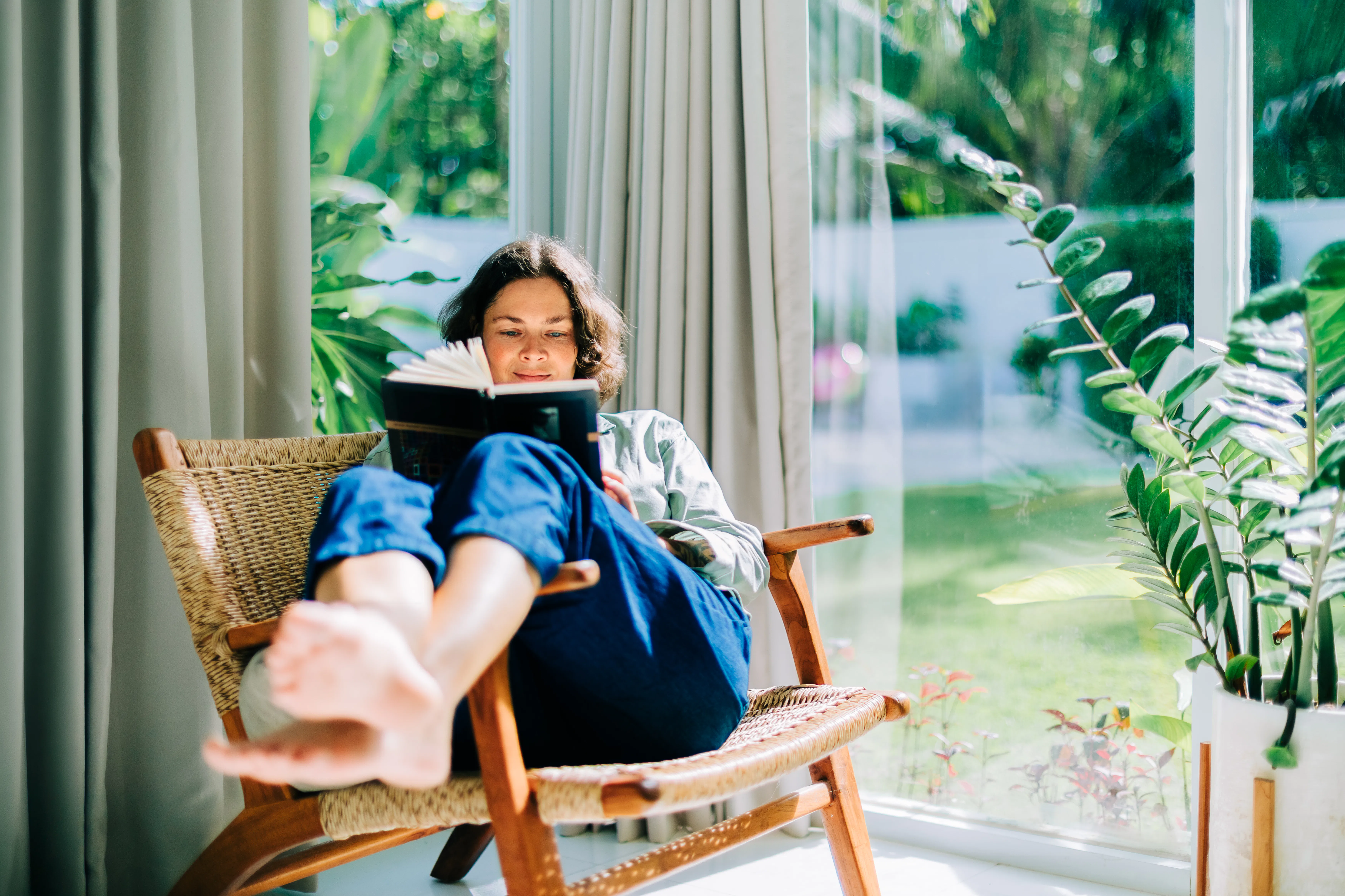 Woman enjoying reading book in armchair by window