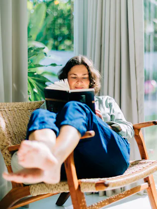 Woman enjoying reading book in armchair by window