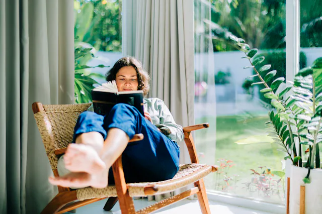Woman enjoying reading book in armchair by window