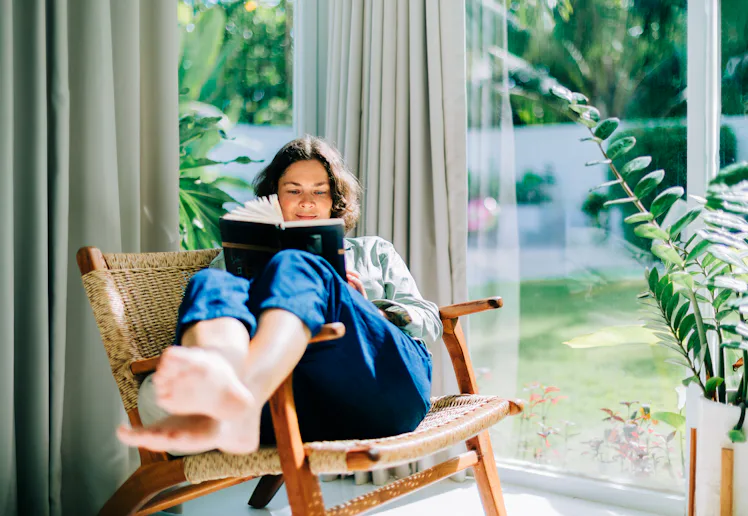 Woman enjoying reading book in armchair by window