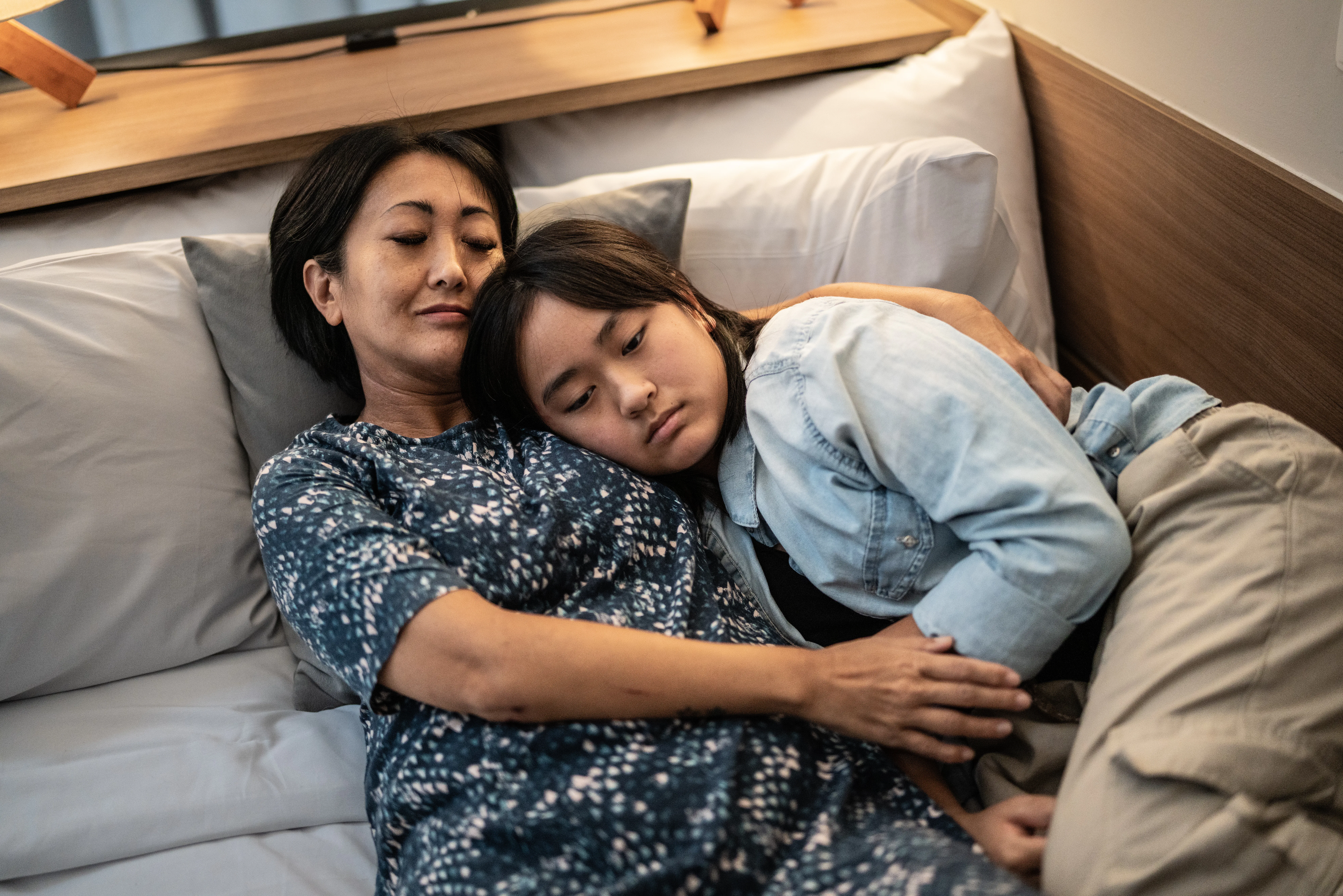 Mother laying down with daughter in bed at home