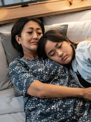 Mother laying down with daughter in bed at home