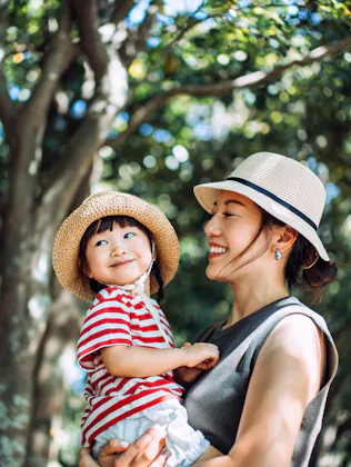 A loving young Asian mother carrying her cute little girl in arms, enjoying nature while spending qu...