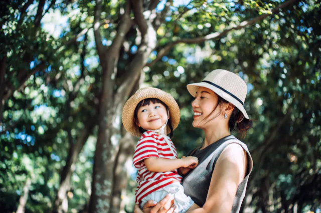 A loving young Asian mother carrying her cute little girl in arms, enjoying nature while spending qu...