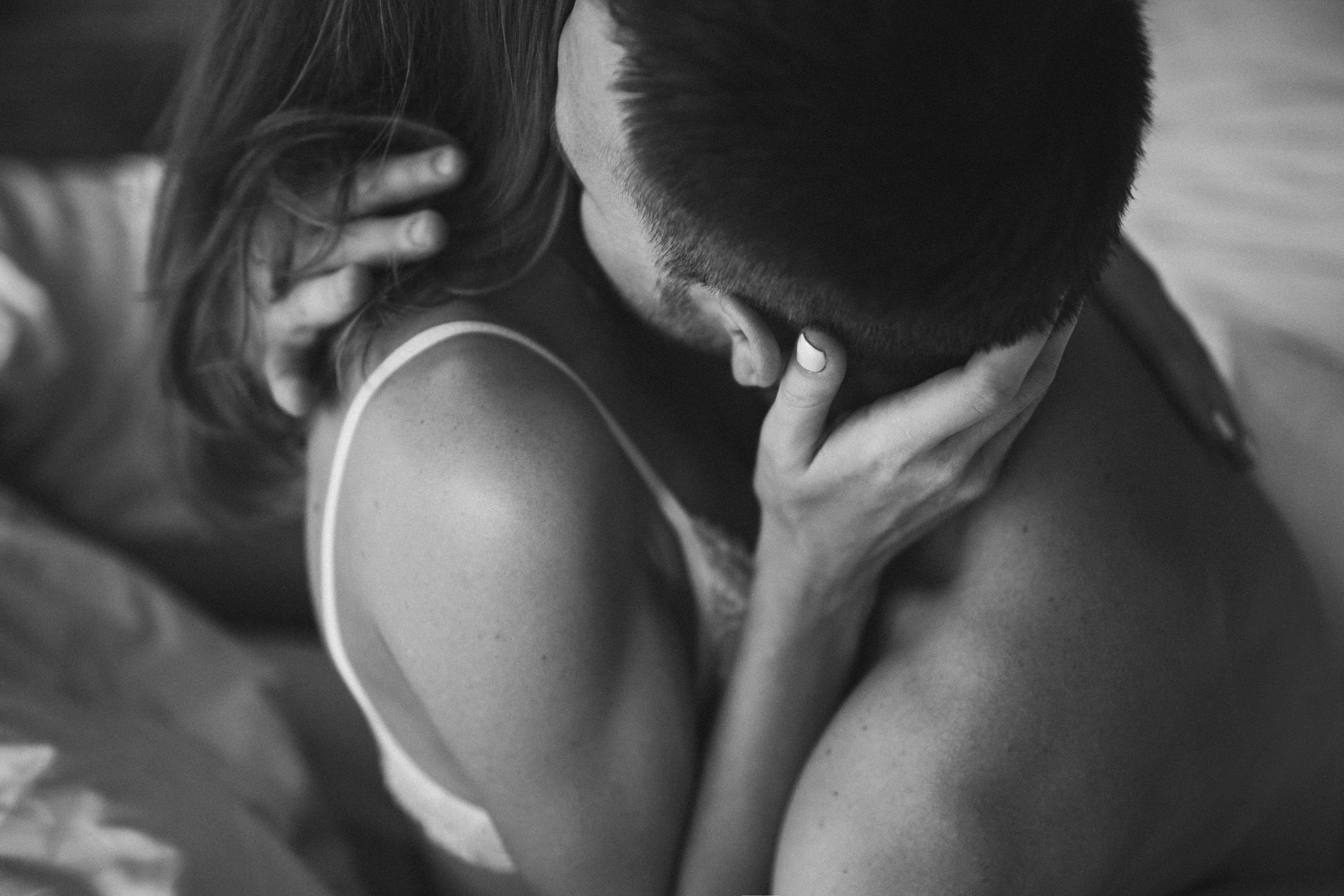 Intimate couple in bed. Kissing with passion and desire. Young lovers on honeymoon. View from behind...