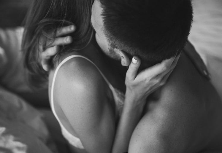 Intimate couple in bed. Kissing with passion and desire. Young lovers on honeymoon. View from behind...