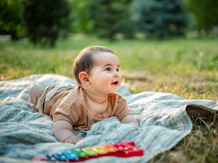 Happy baby boy playing on a picnic blanket in nature, surrounded by lush greenery. Joyful childhood ...